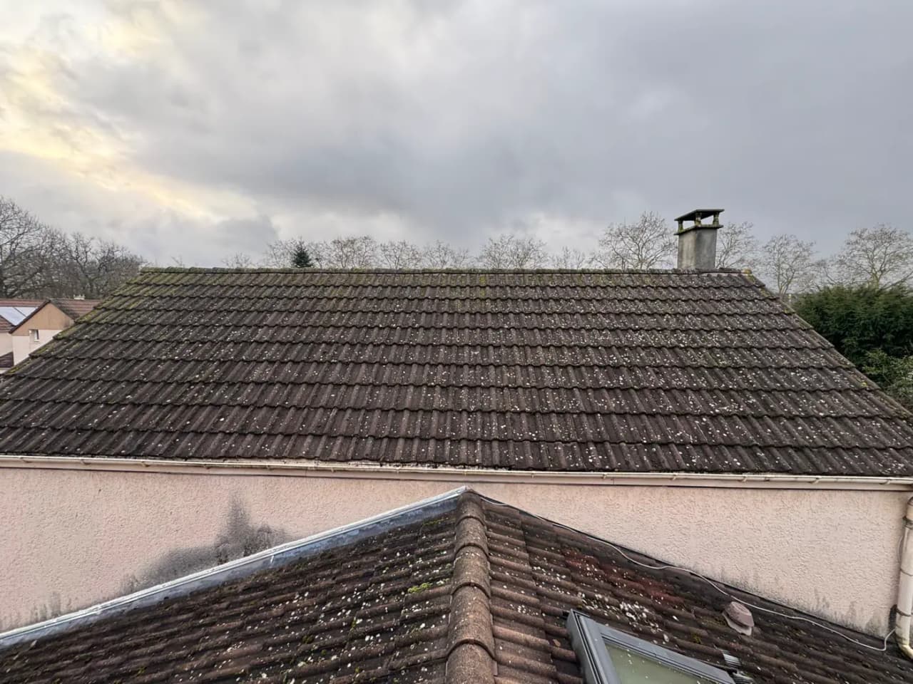 Toiture en tuiles couverte de mousse sous un ciel gris, avant démoussage